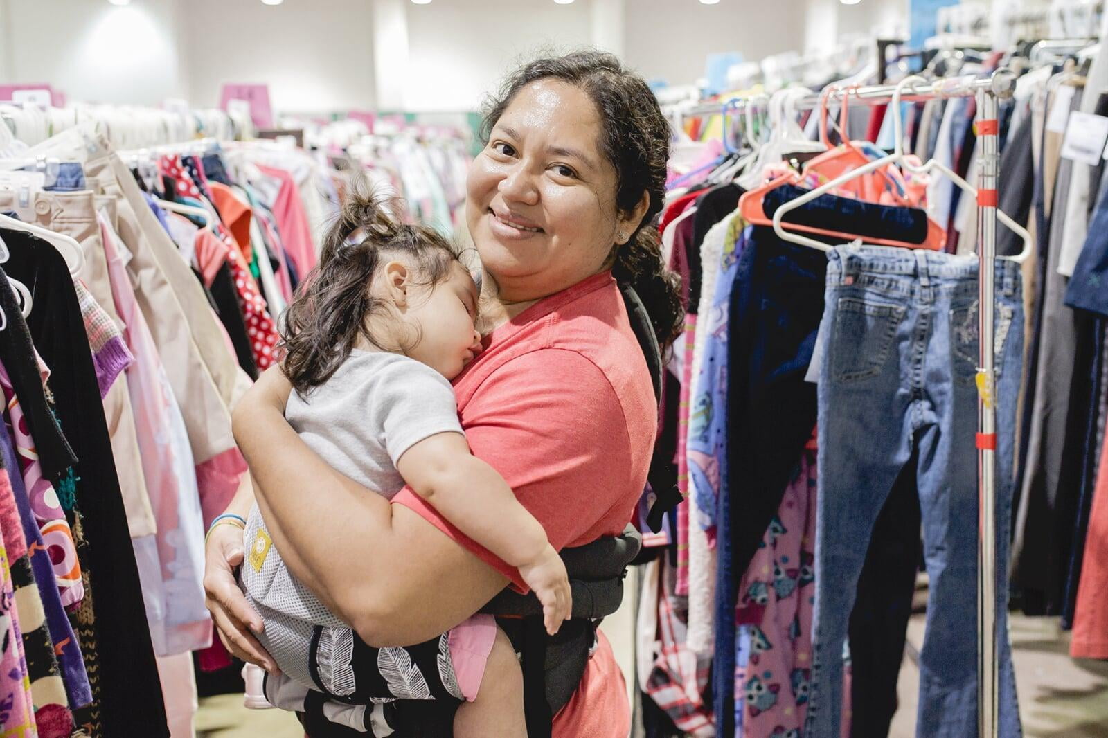 Mom holds daughter who is sleeping in her arms while she shops the local JBF sale.